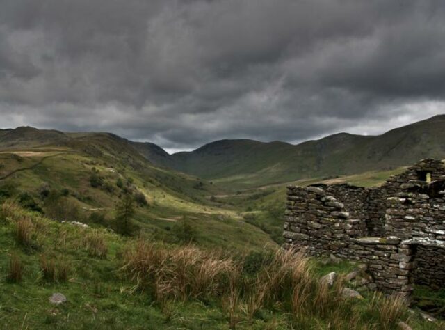 Rolling landscape with storm clouds in the background and stone bothy in the foreground