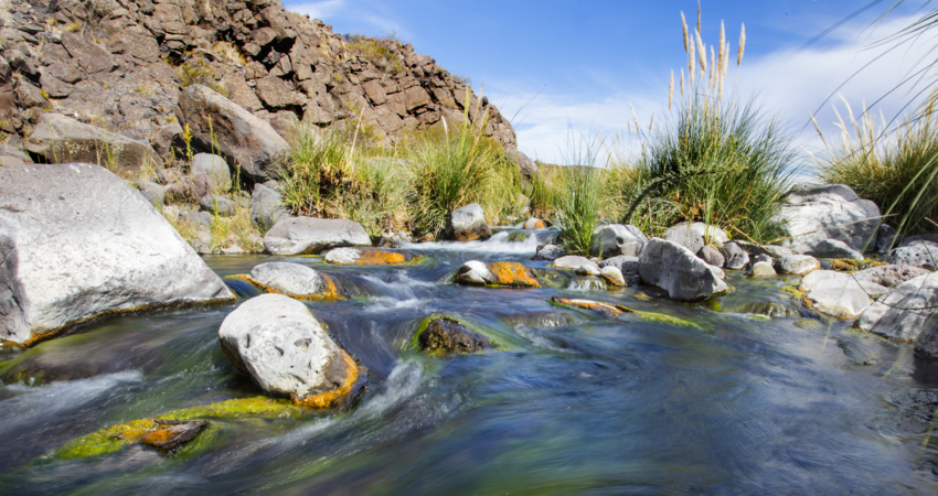 The headwaters of the Valcheta stream, surrounded by rocky landscape, beneath a sunny blue sky